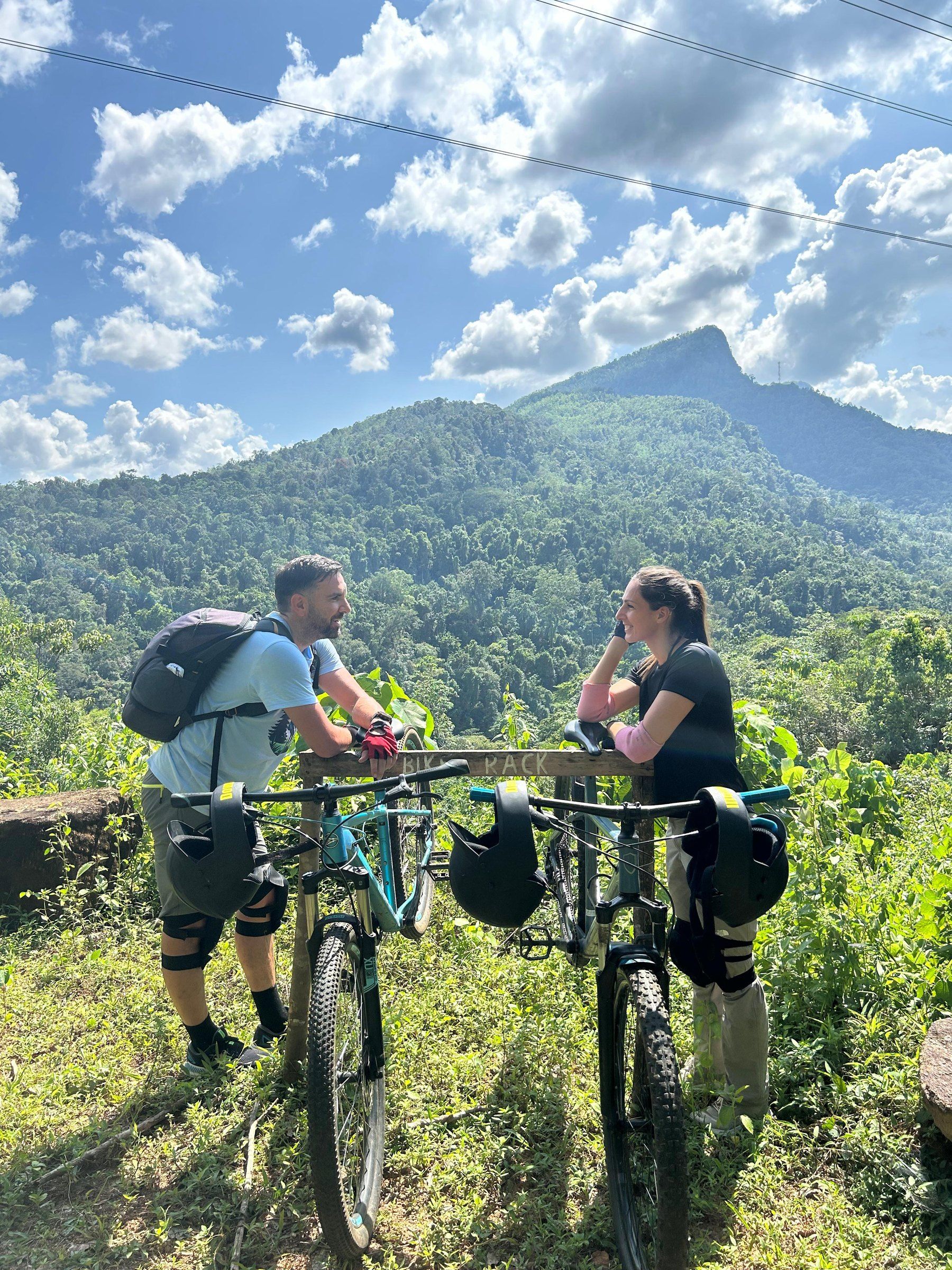 Two riders rest on their bikes at the view point and look at each other