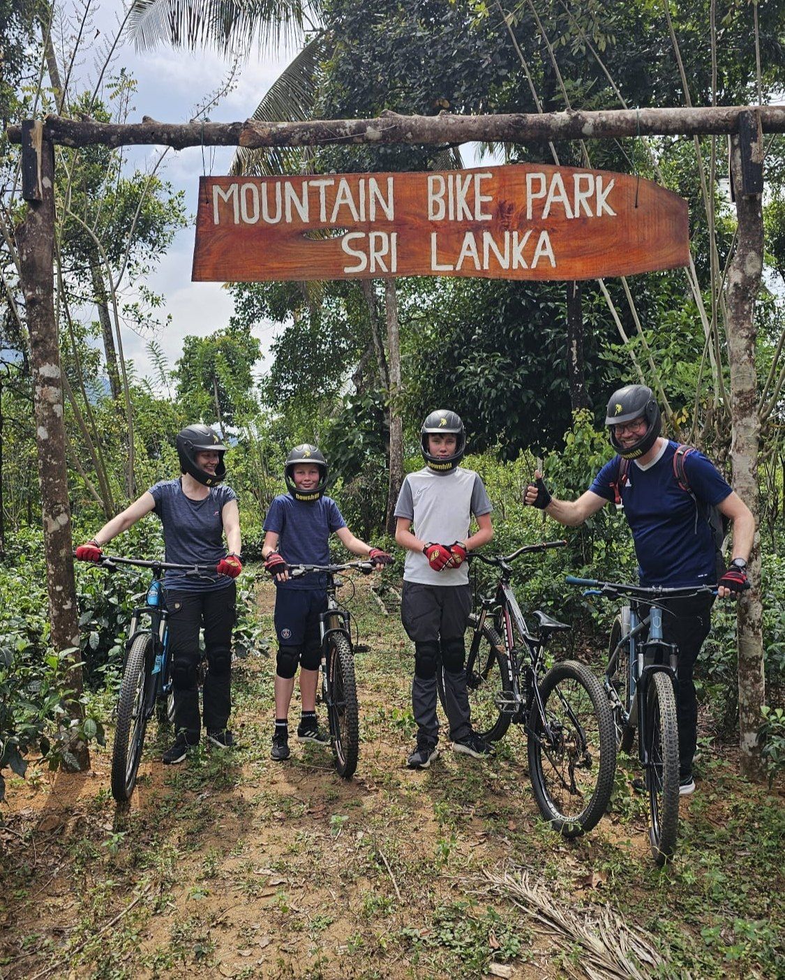 Four riders line up with their bikes under the Mountain Bike Park Sri Lanka sign